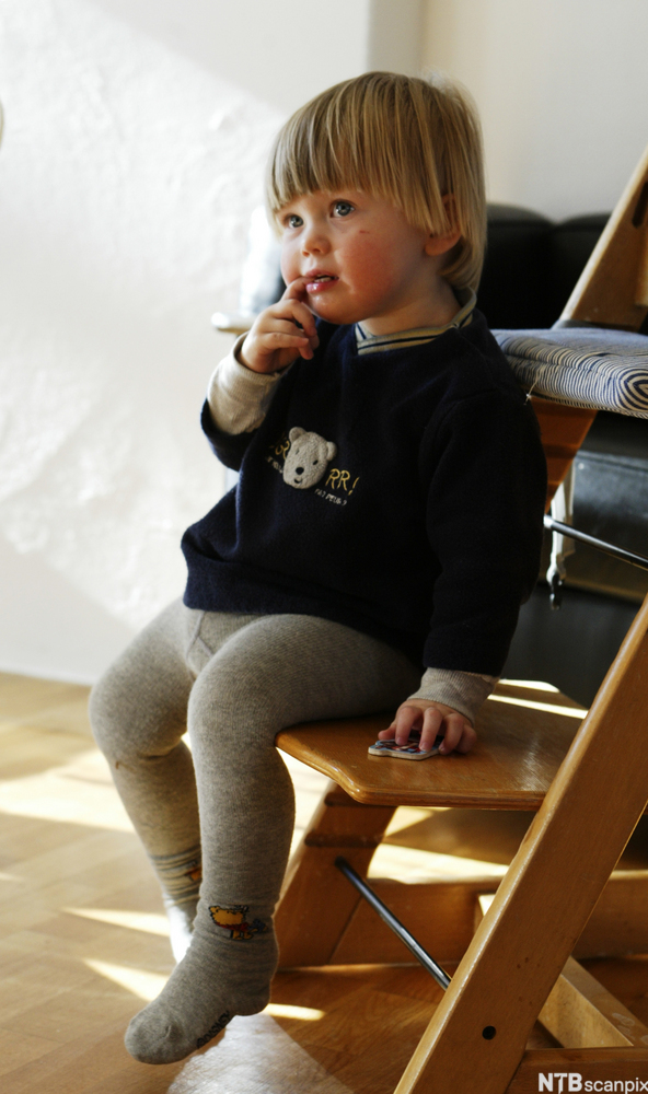 Et lite barn sitter på stol. Foto.