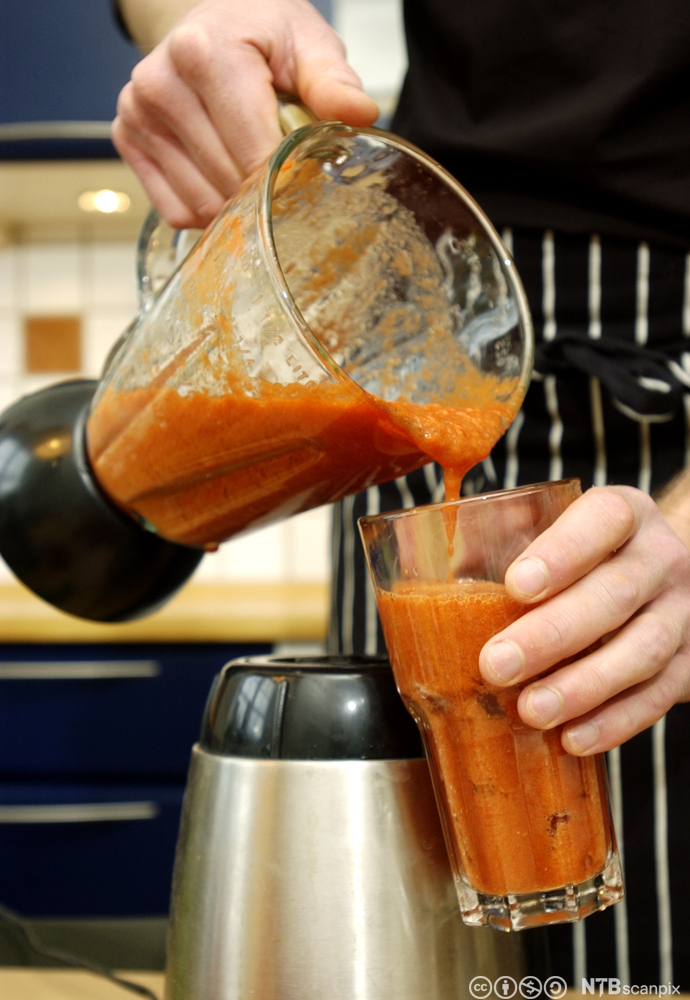 Rød gazpachosuppe helles fra en blender ned i et stort glass. Foto.