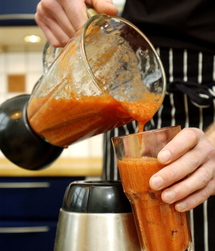 Rød gazpachosuppe helles fra en blender ned i et stort glass. Foto.