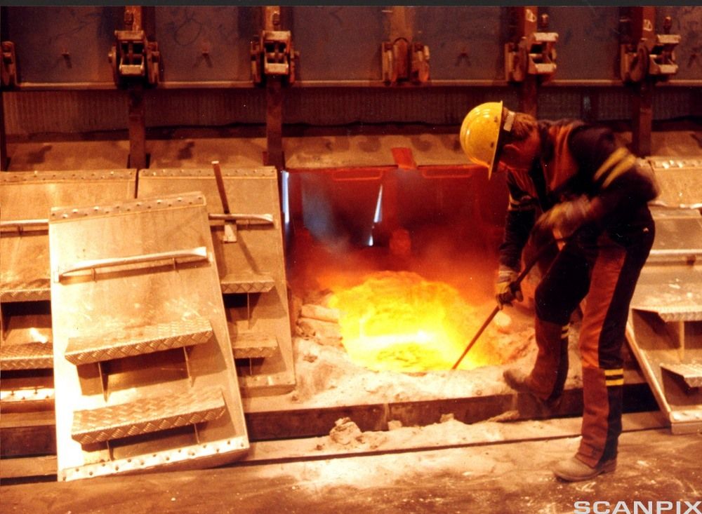 Mann med hjelm og annet verneutstyr i arbeid med smelting av aluminium. Foto.