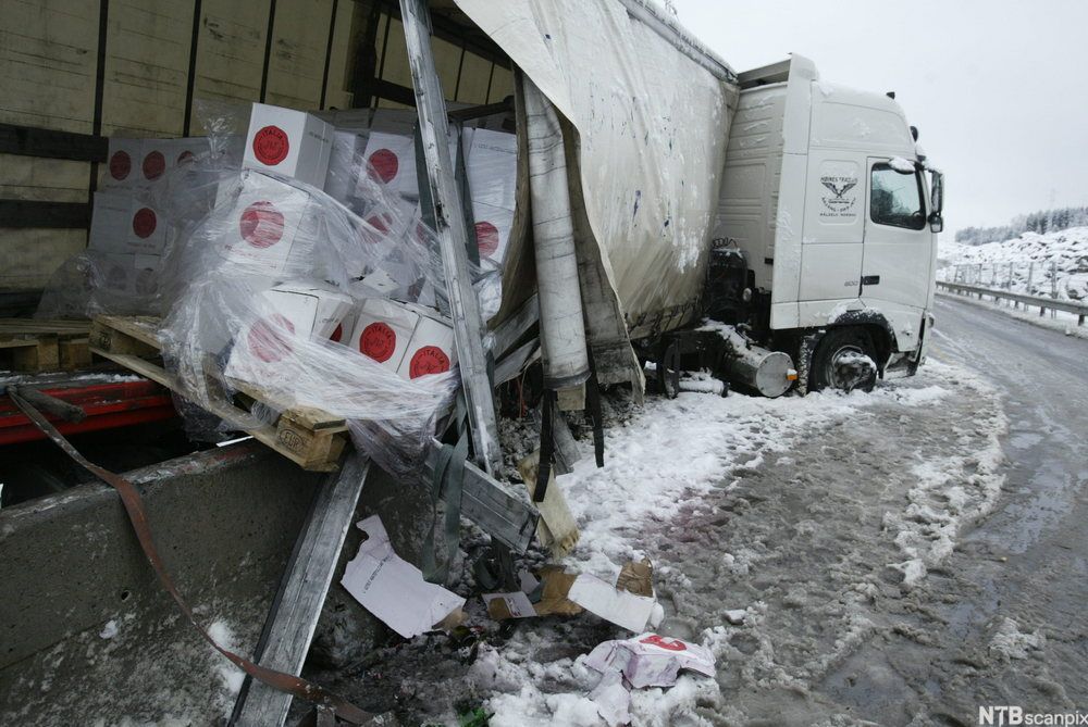 En lastebil har krasjet i grøfta i snøværet. Bilen er flerret opp, og emballerte varer har ramlet fra en pall og ut i snøen. Bilde.