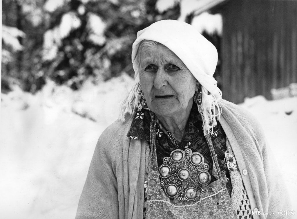 Portrett av en eldre kvinne. Hun har skaut, øredobber og stor sølje. Foto. 