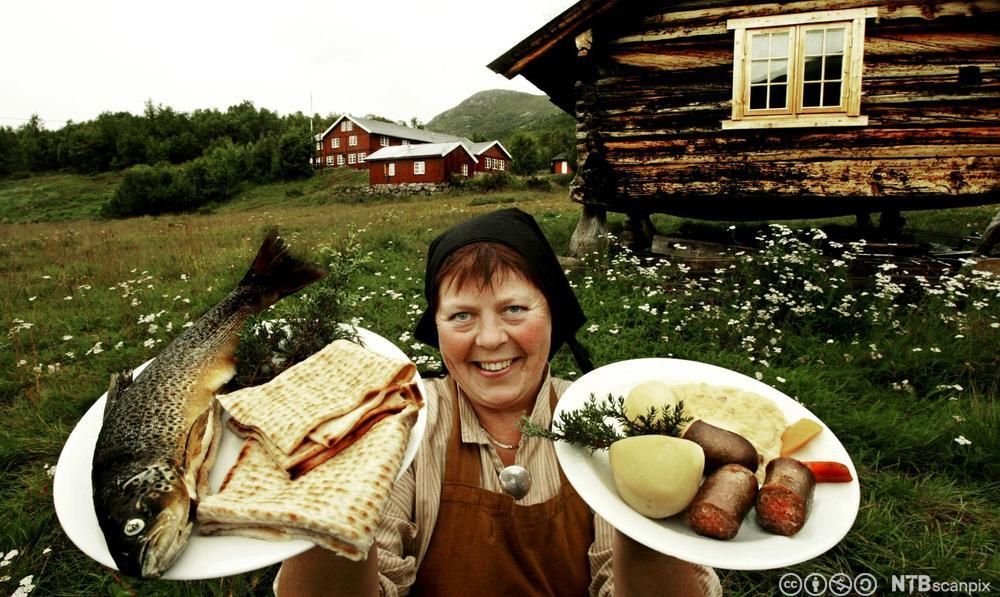 Bilde av en dame på en gård med to fat lokalmat. Foto.