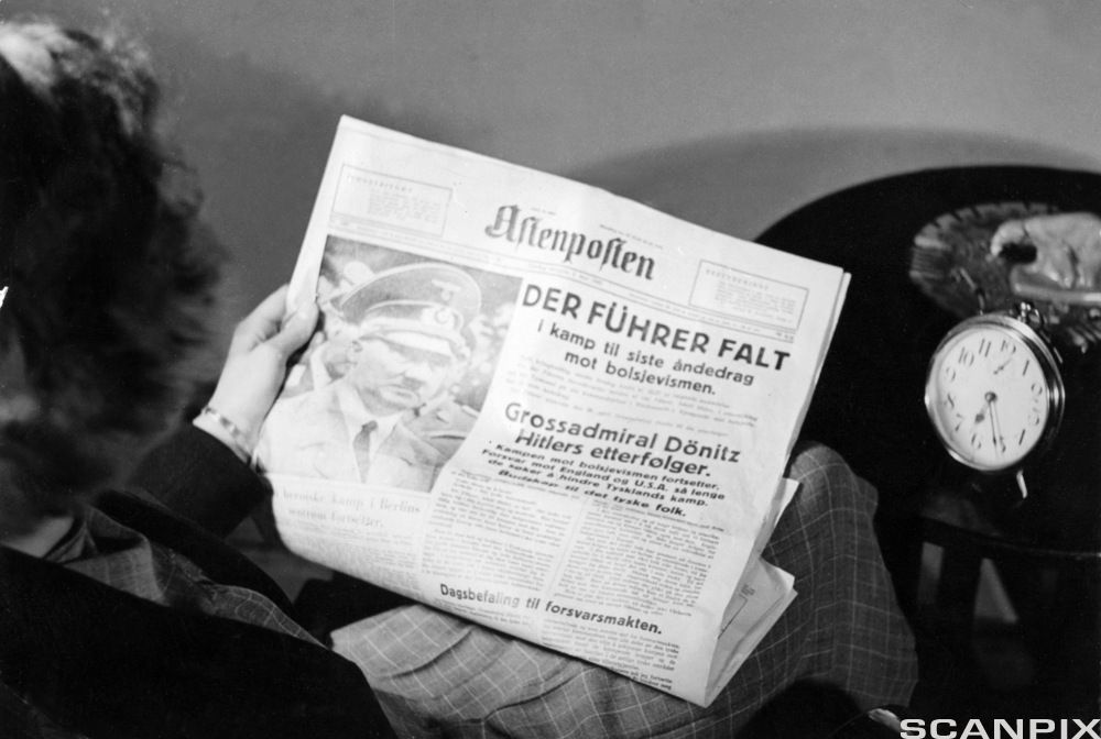 En kvinne sitter i en bil og leser Aftenposten. Forsideoppslaget handler om at Hitler er død, og ifølge oppslaget falt han "i kamp til siste åndedrag mot bolsjevismen". Foto.