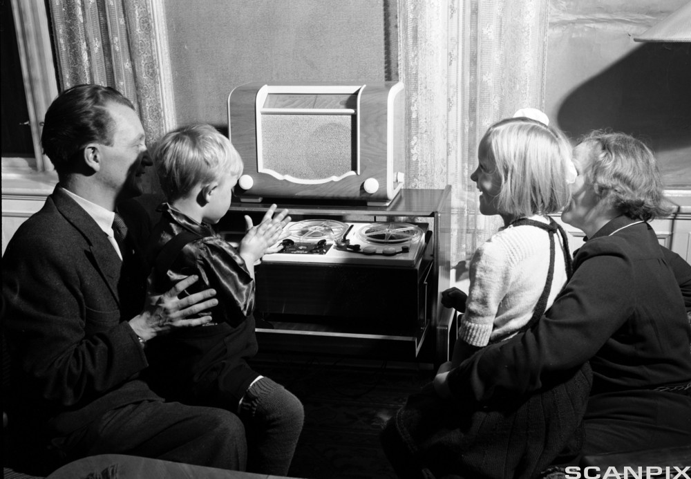 En familie lytter til radio i fellesskap en gang på 1950-tallet. Bilde.
