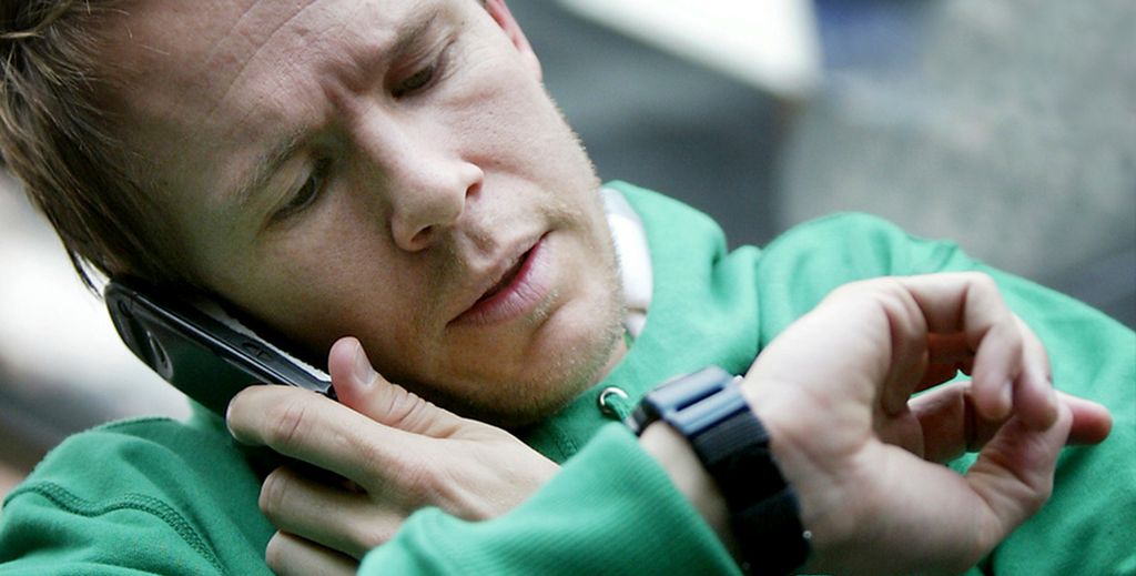 Mann ser på klokka mens han snakkar i mobiltelefon. Foto.