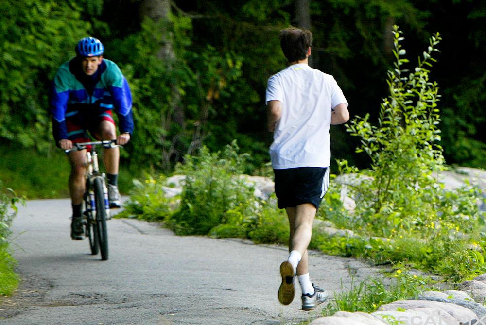 En syklende og en joggende langs landevei. Foto.