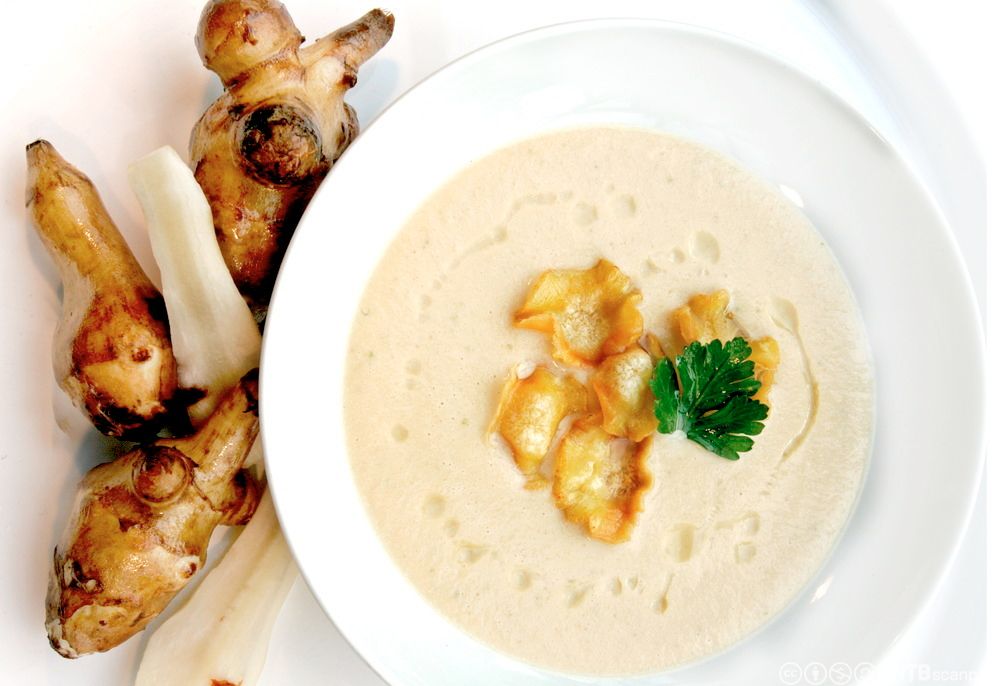 En tallerken med jordskokksuppe, dandert med stekte skiver av jordskokk og et persilleblad. Foto.