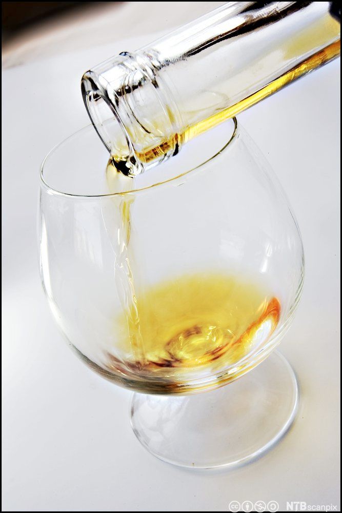 Ein som heller konjakk frå ei flaske og i eit glas. Foto.