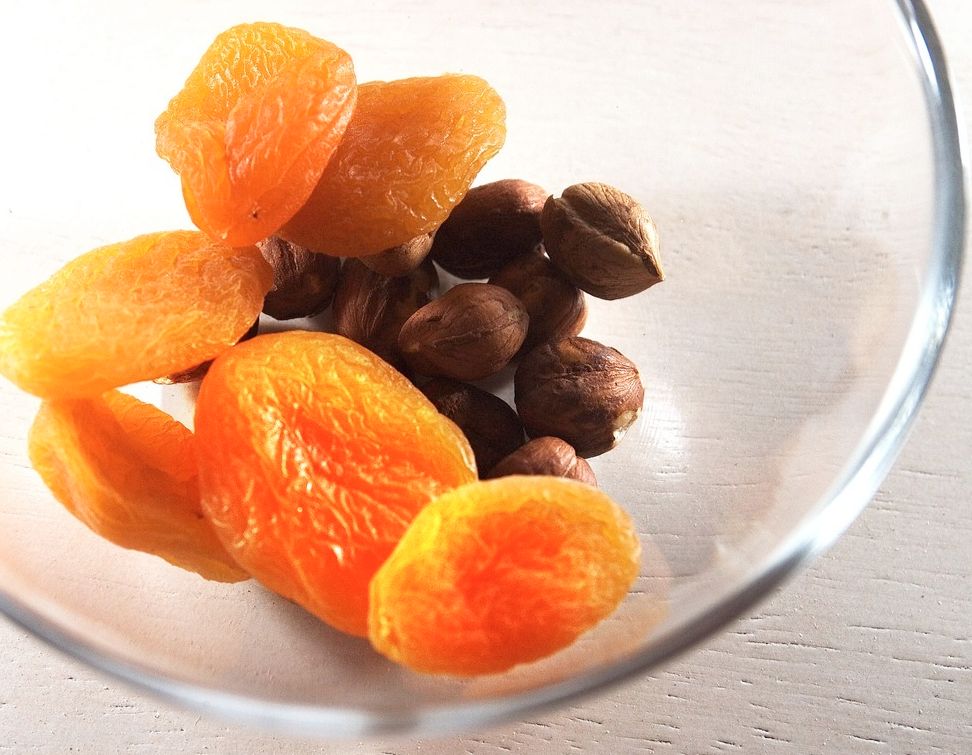 Tørka aprikosar som ligg litt føre nokon nøtter i eit blank glas skål. Foto.