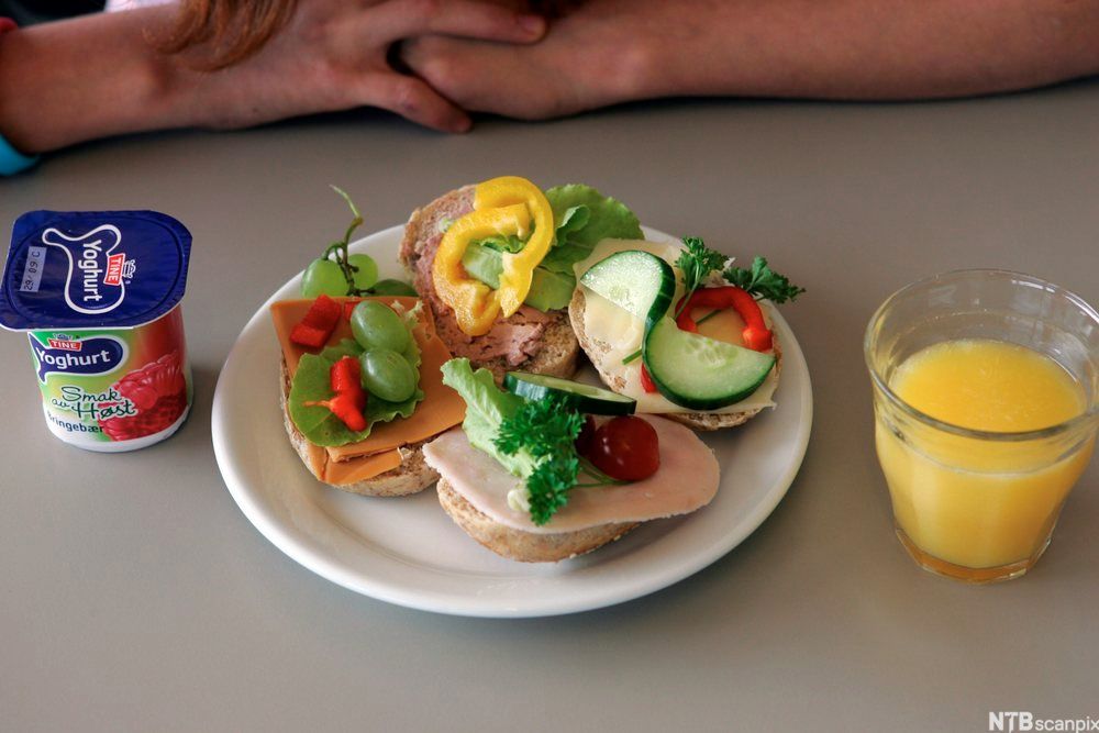 Frokost som består av yoghurt, rundstykker med pålegg og et glass juice. Foto.