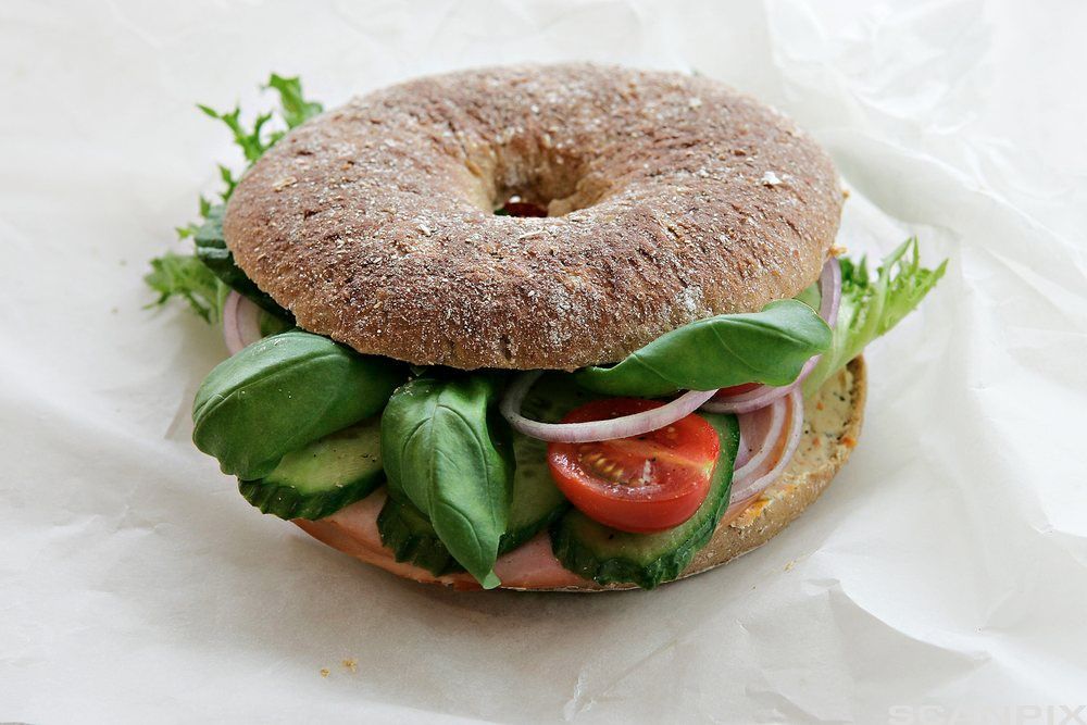 En grov bagel med agurk, salat, løk og tomat. Foto.