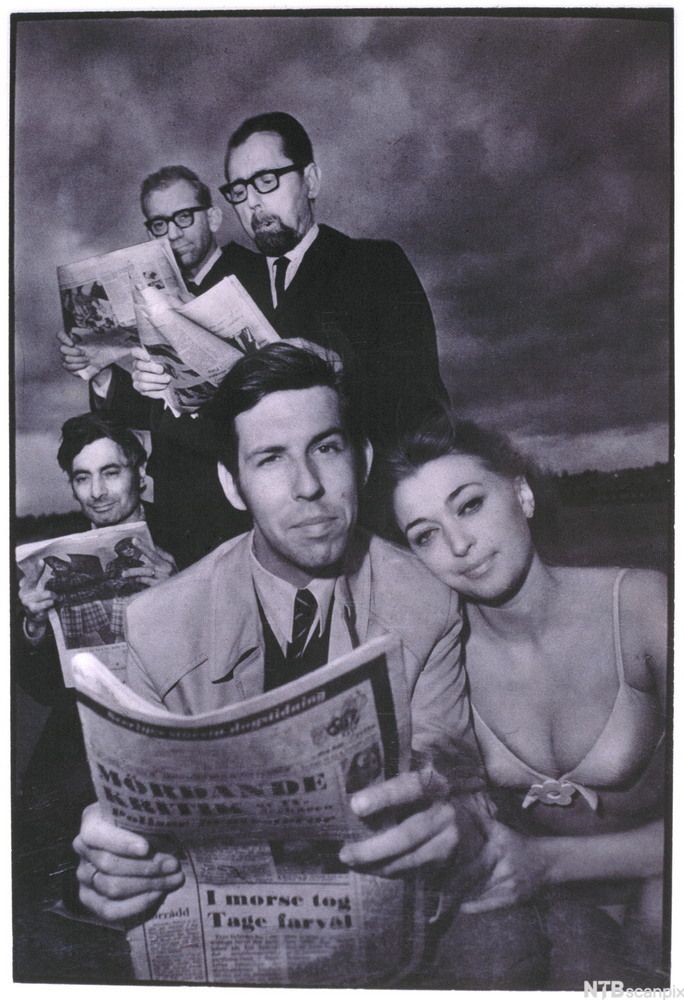 Dresskledde menn les aviser, og en kvinne i bikini lener seg inntil den fremste av dem. Foto.