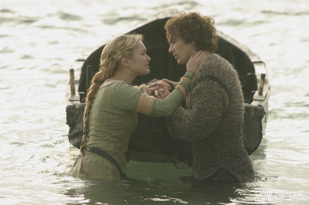 Tristan og Isolde står ved ein pram, nokon meter uti vatnet, og held hendene til kvarandre. Stillbilete frå film.