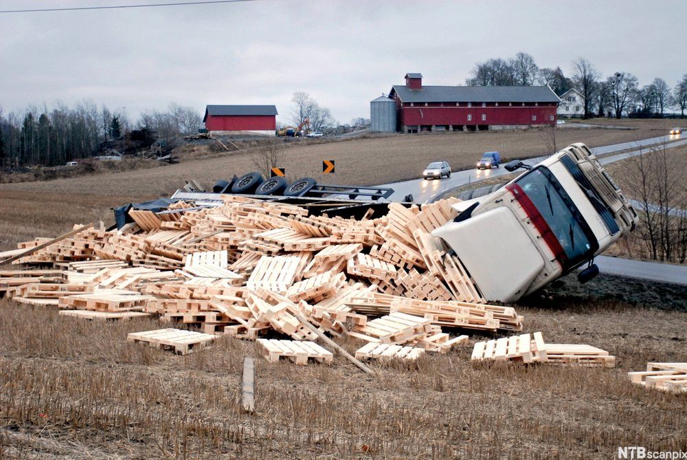 Et vogntog lastet med paller har veltet i en sving. Paller flyter utover bakken. Foto.