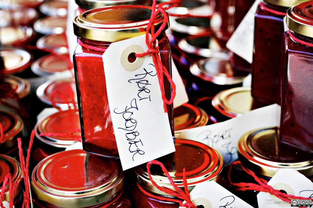 Mange glass med rørt jordbær, merket med håndskrevne lapper festet med rødt bånd. Foto.