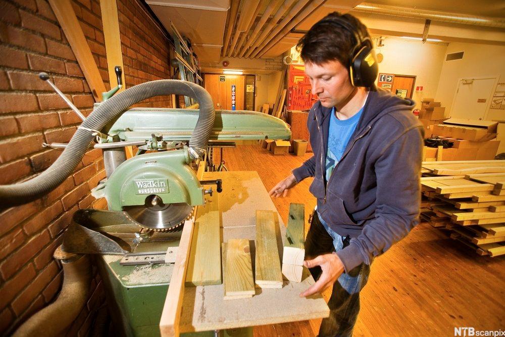 En mann står ved ei sag, han har kuttet opp impregnerte bord. Foto.