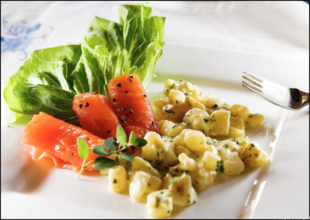 Skiver av gravlaks med stuet potet og noen salatblader på en tallerken. Foto.