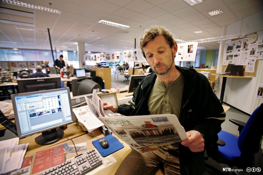 Mann leser avis i redaksjonslokale. Fotografi.