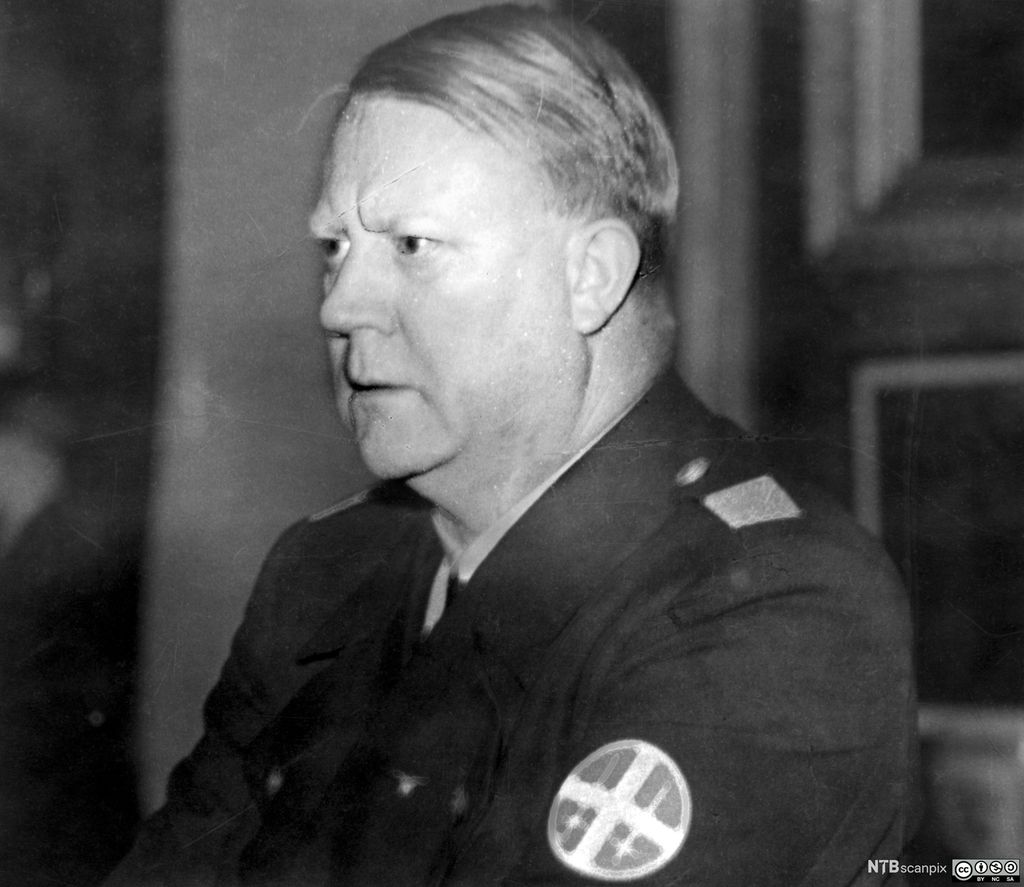 Et portrett av Vidkun Quisling i femtiårsalderen. En noe overvektig mann med glatt, kortklipt, mellomblondt hår. Han har på seg NS-uniform, ser rett fram og virker konsentrert og alvorlig. Han har ei dyp vertikal rynke mellom øynene. Foto.