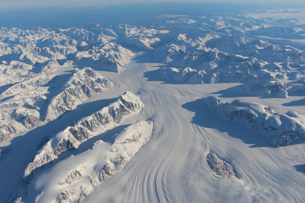 Flyfoto av en stor isbre som ligger mellom snødekte fjelltopper. Foto. 