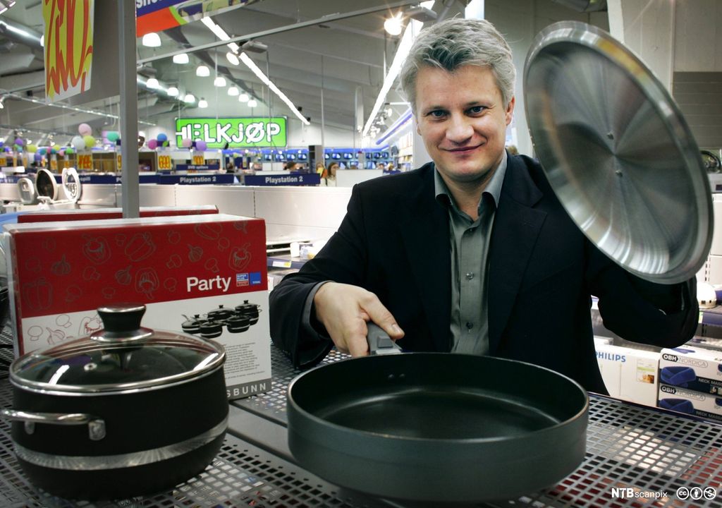 En mann viser fram en stekepanne med lokk som står utstilt i en butikk. Foto.