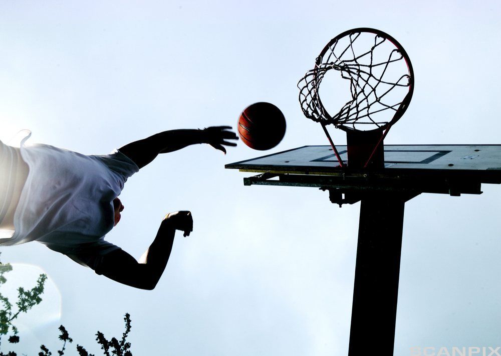 Mann kaster basketball mot basketballkurv. Foto i froskeperspektiv.