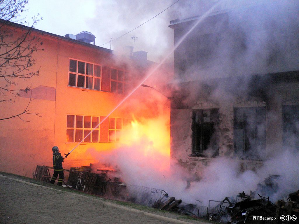 Brannmann slukker brann på utsida av en stor bygning. Foto.