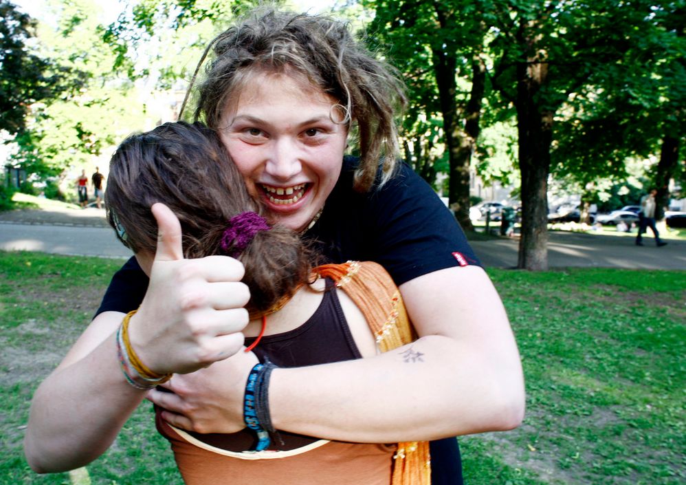 To personer som gir hverandre en god klem. Den ene ser inn i kameraet og viser tommel opp. Foto.