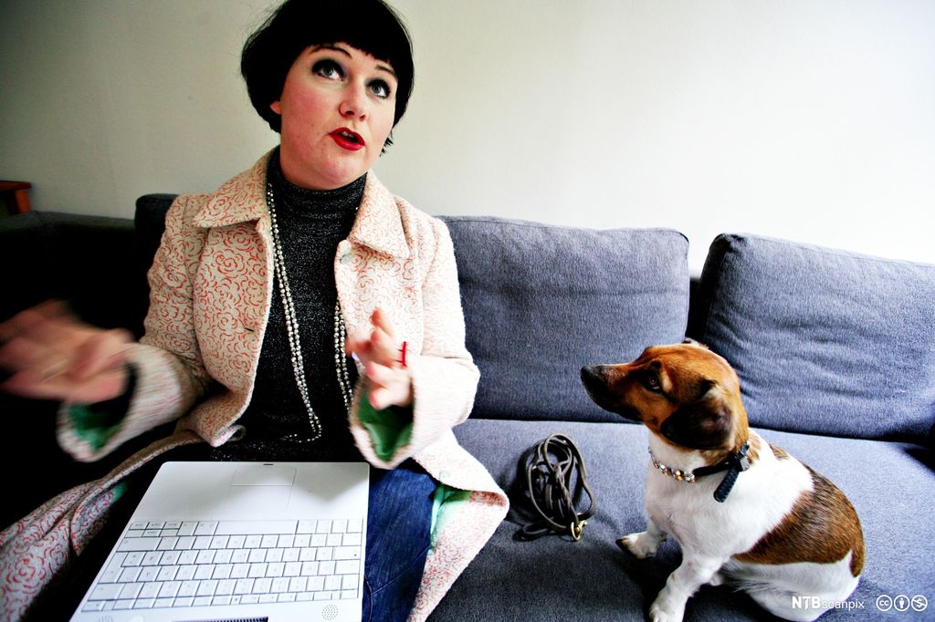 Christine Koht på sofaen hjemme, med laptop i fanget og hunden Pippi ved sida av seg. Foto.