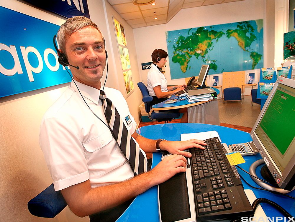 Ung mann som jobber i et reisebyrå, med datamaskin og hodetelefon. Foto.