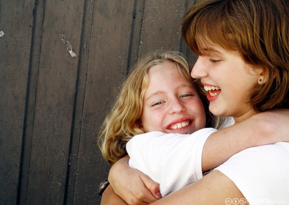 Glade søstre holder rundt hverandre. Foto.