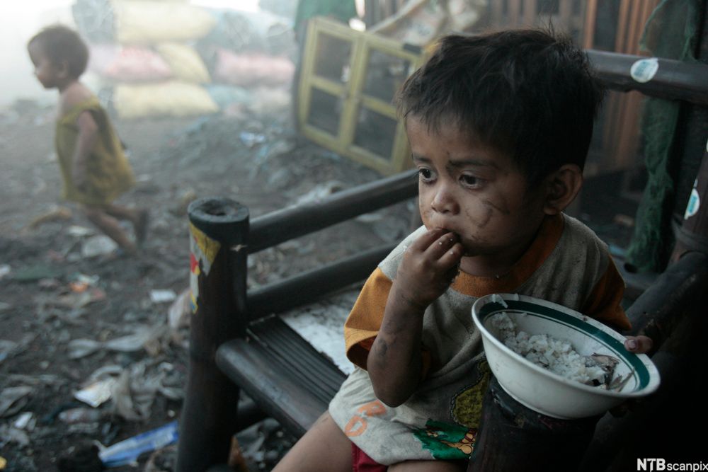 En fattigslig gutt spiser ris fra en bolle. Foto.