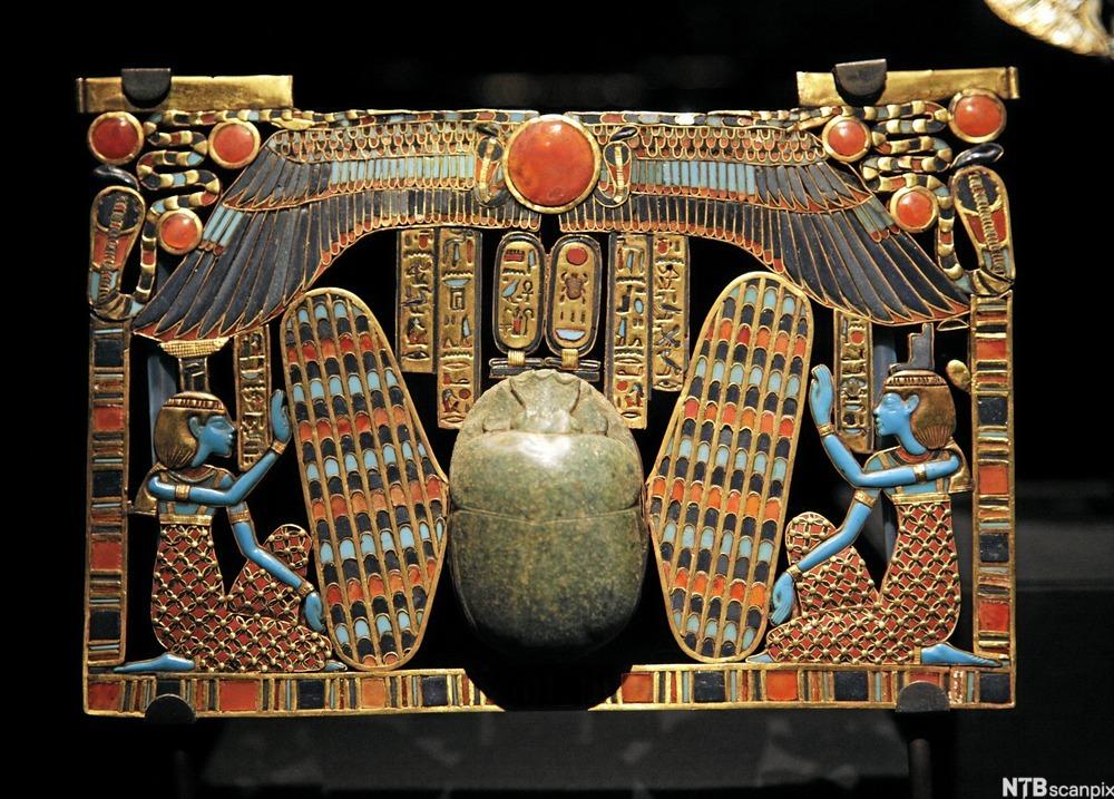 Pectoralsmykke i gull med røde, blå og svarte dekorasjoner. Foto.