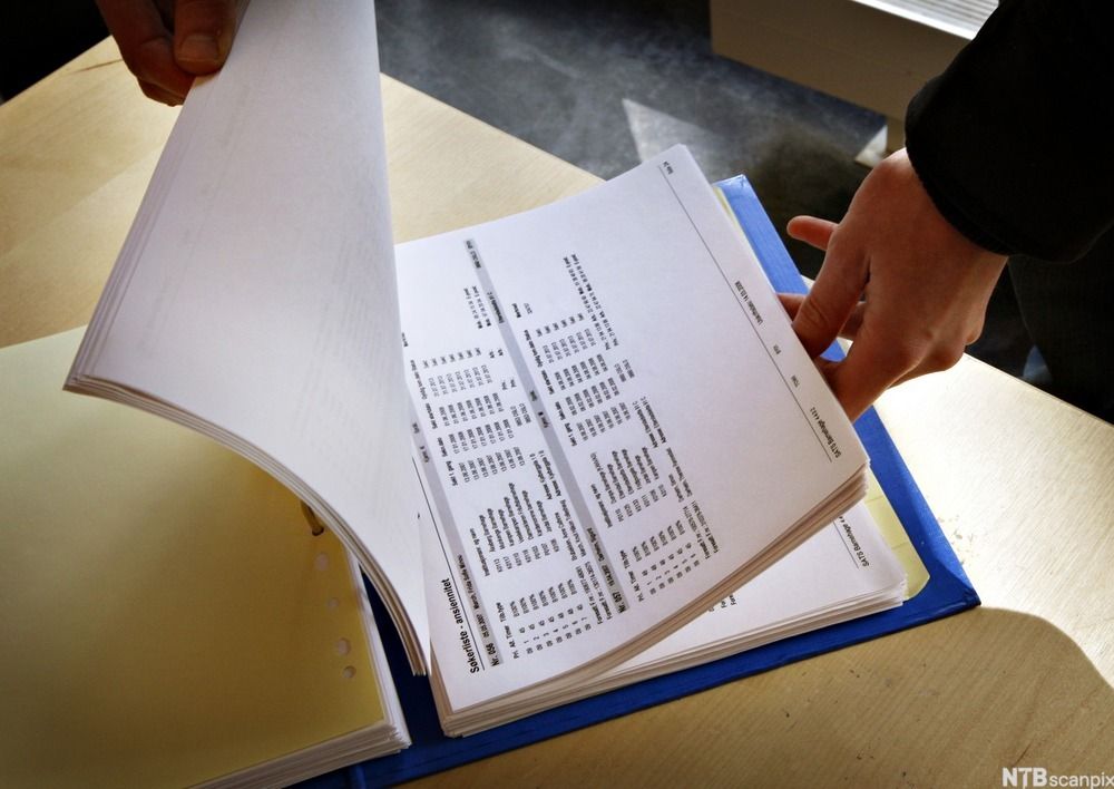 Person ser gjennom papirer i en perm. Foto.