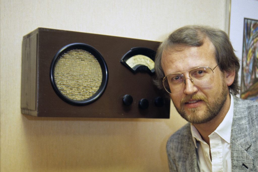 Mann lytter til gammelt radioapparat. Foto.