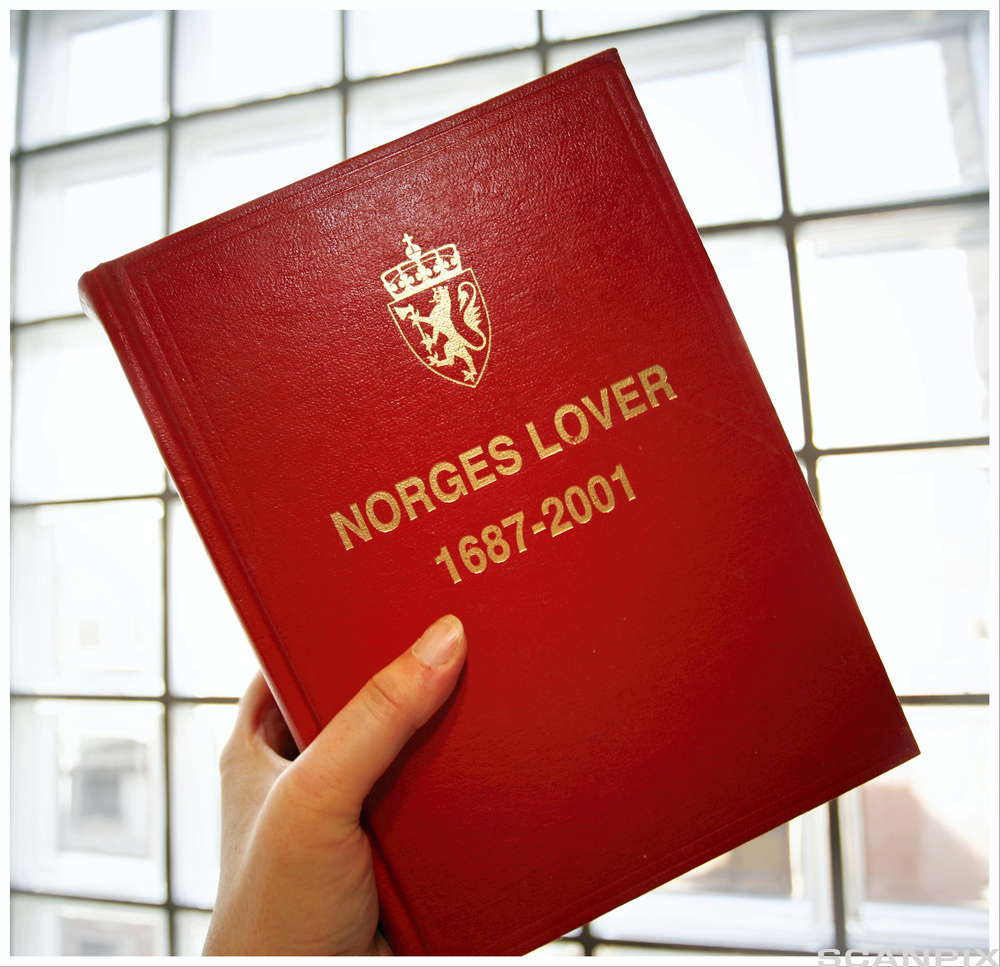 Hånd som holder boka Norges lover. Foto. 