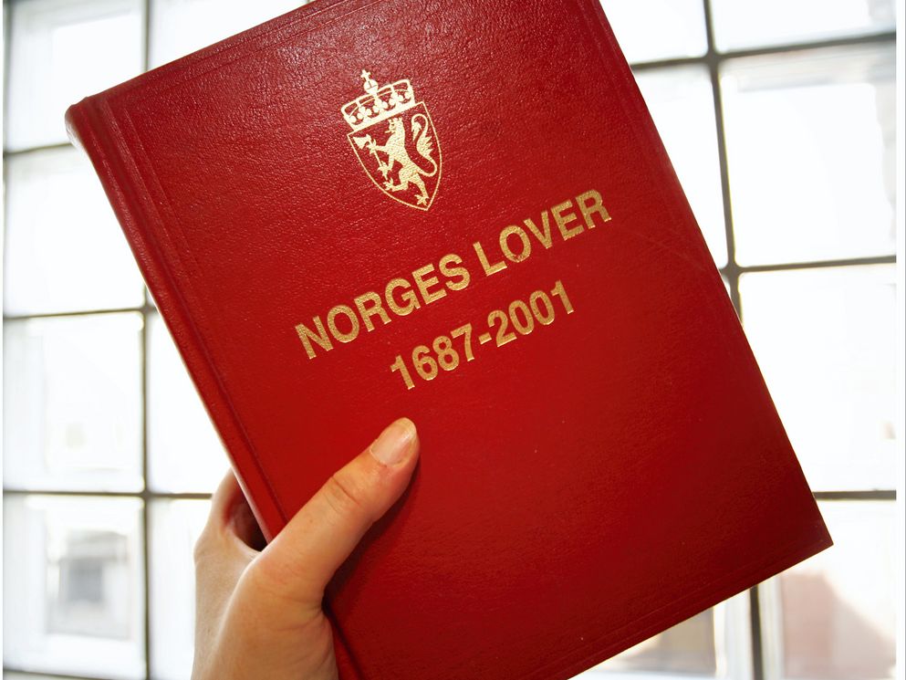 Hånd som holder boka Norges lover. Foto.