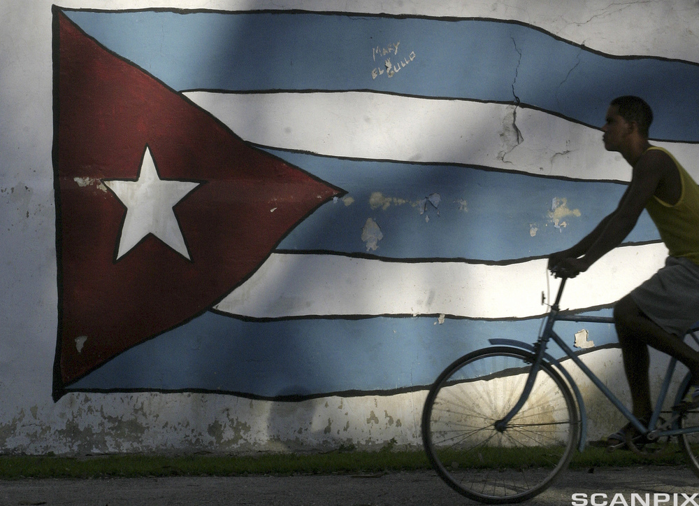 Ein mann syklar forbi det kubanske flagget i Havana. Foto.