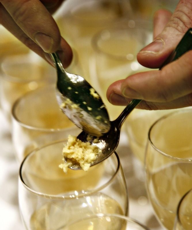 En person skraper revet ingefær fra en skje ned i et glass. Foto.