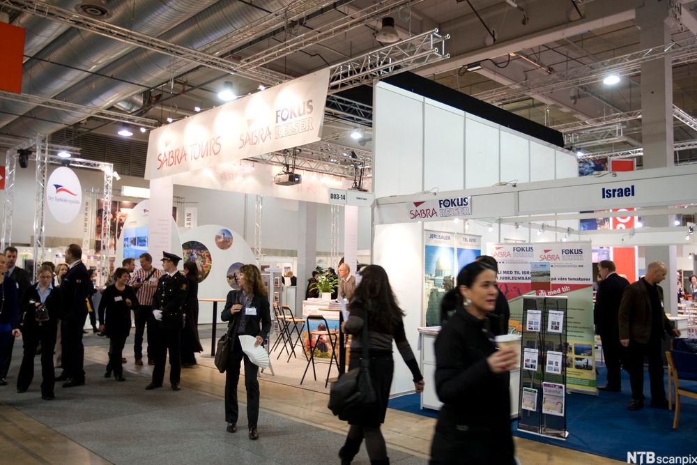 På Reiselivsmessen 2009 på Lillestrøm. Flere personer beveger seg rundt i en messehall. De har alle navneskilt på brystet. Langs mingleområdet er det hele veien stander med aktører som presenterer reiseproduktet sitt. Foto.