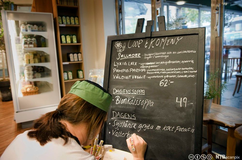 Kokk skriver opp dagens økologiske meny på en tavle. Foto.