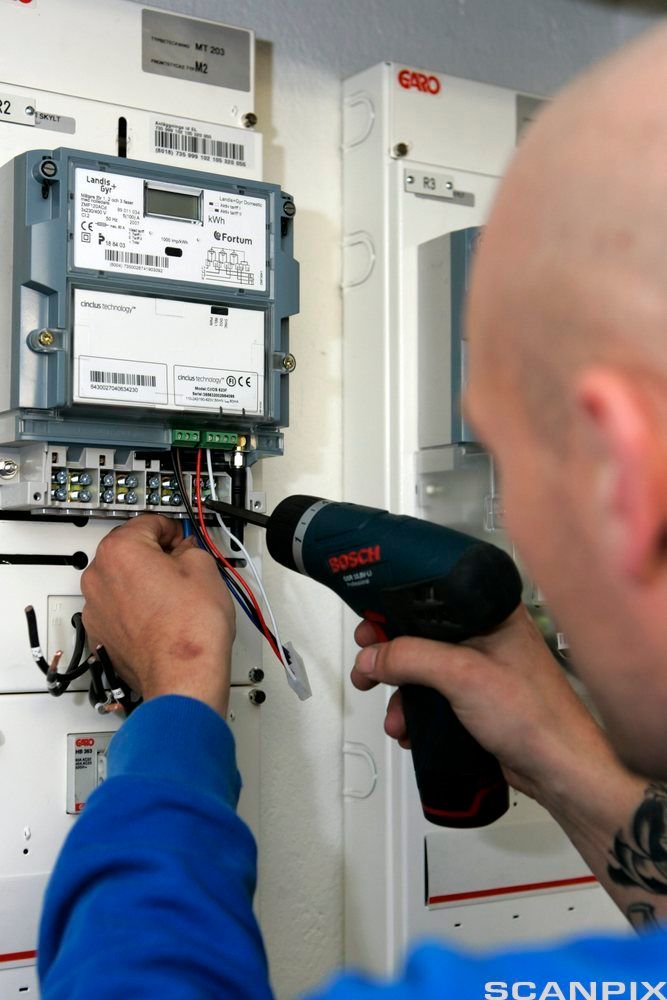 En montør skrur på plass en digital strømmåler. Foto.