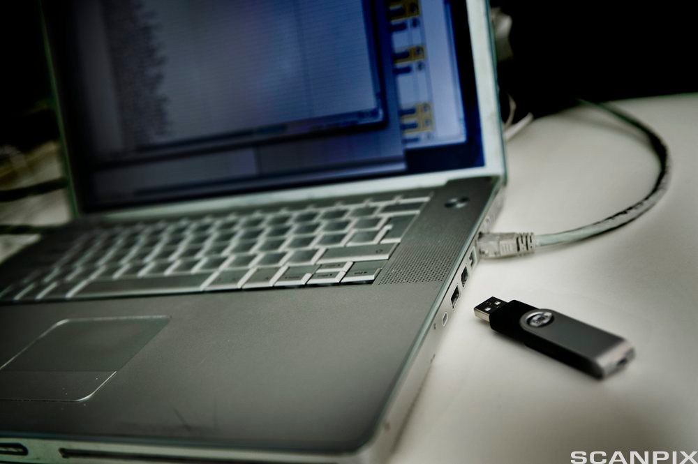 Bærbar datamaskin fotografert fra siden. En USB-minnepinne ligger ved siden av. Foto.