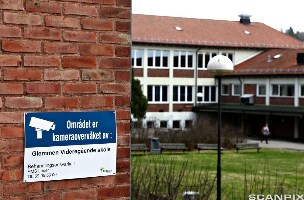 Skolebygg med et skilt på en vegg som opplyser om at området er kameraovervåket. Foto.