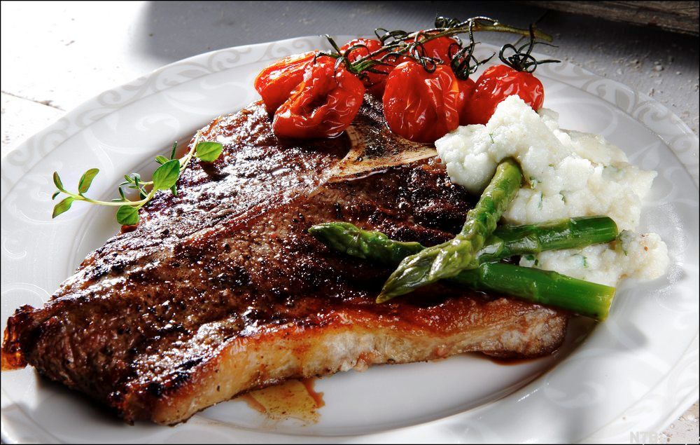 Stekt kjøttstykke med tomater, asparges og sellerirotpuré servert på hvit tallerken. Foto.