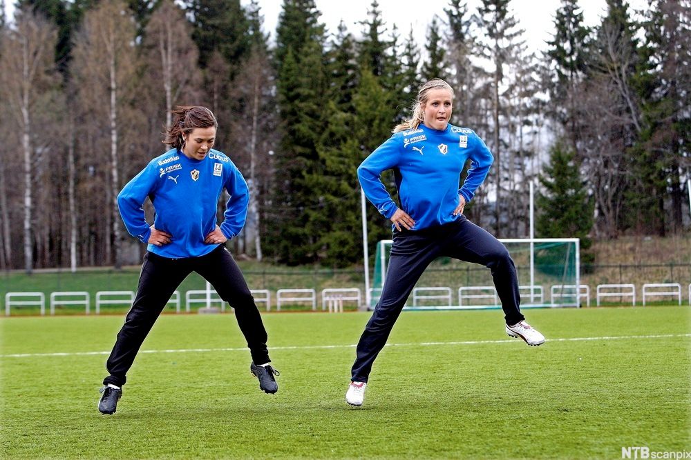 To unge kvinner varmer opp på en fotballbane. Foto.