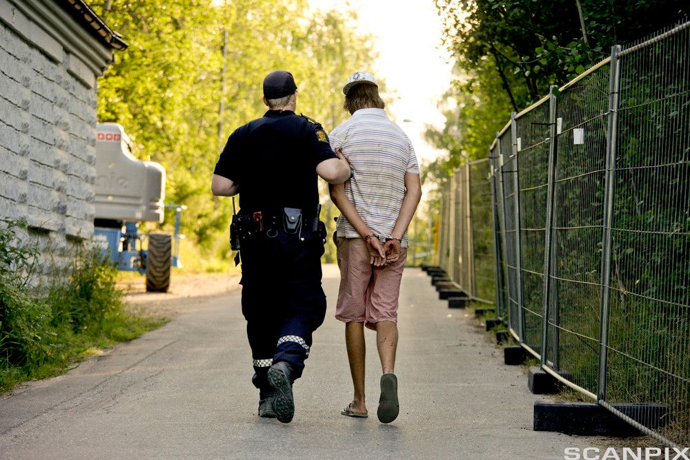 En politibetjent har grepet tak i overarmen til en ung mann og fører han bort fra et festivalområde. Den unge mannen er påsatt håndjern. Foto.