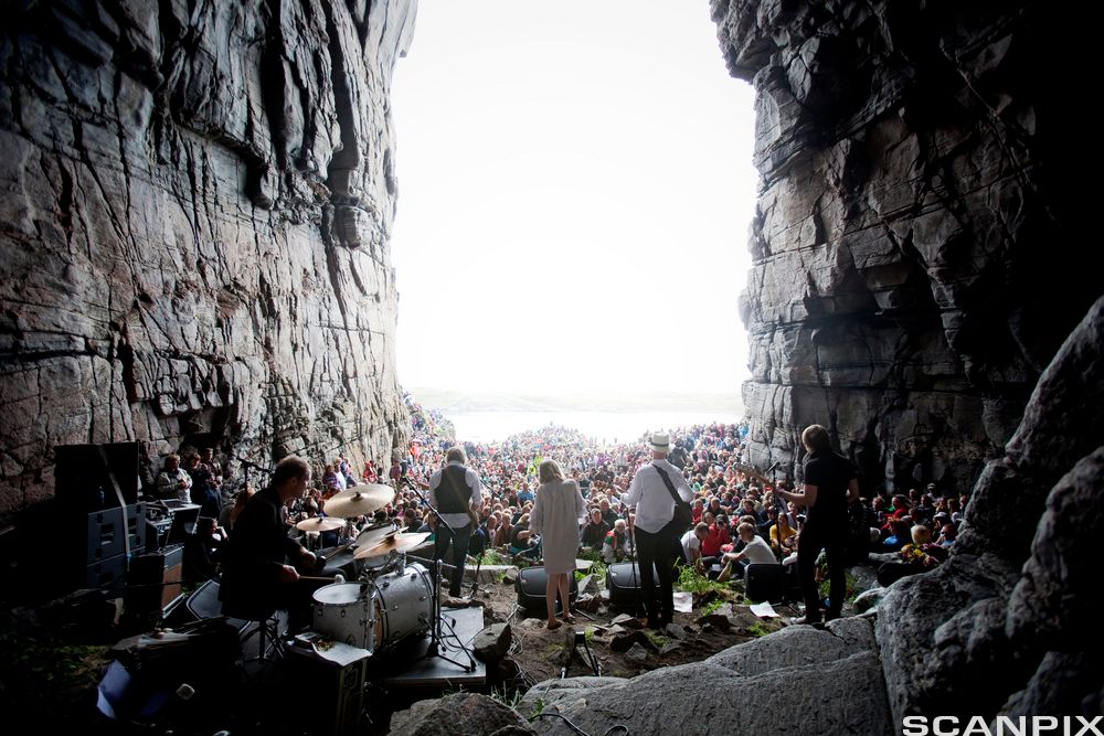 Musikere i en huleåpning foran et stort publikum. Foto.