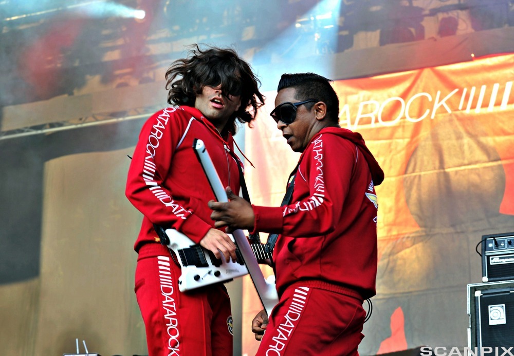 To menn i rød joggedress med teksten "DATAROCK" langs ermet. De har på seg store solbriller og spiller på hvite gitarer på en scene. Foto.